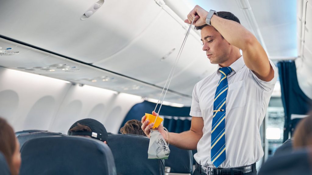 Flight attendant demonstrating how to put on oxygen mask