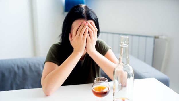 Woman distressed with hands on face next to alcohol