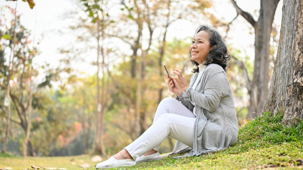 Woman using phone outside sitting by a tree